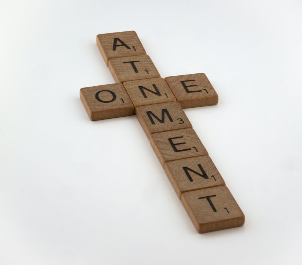 Scrabble tiles arranged in a cross shape spelling 'atonement' on a white background.